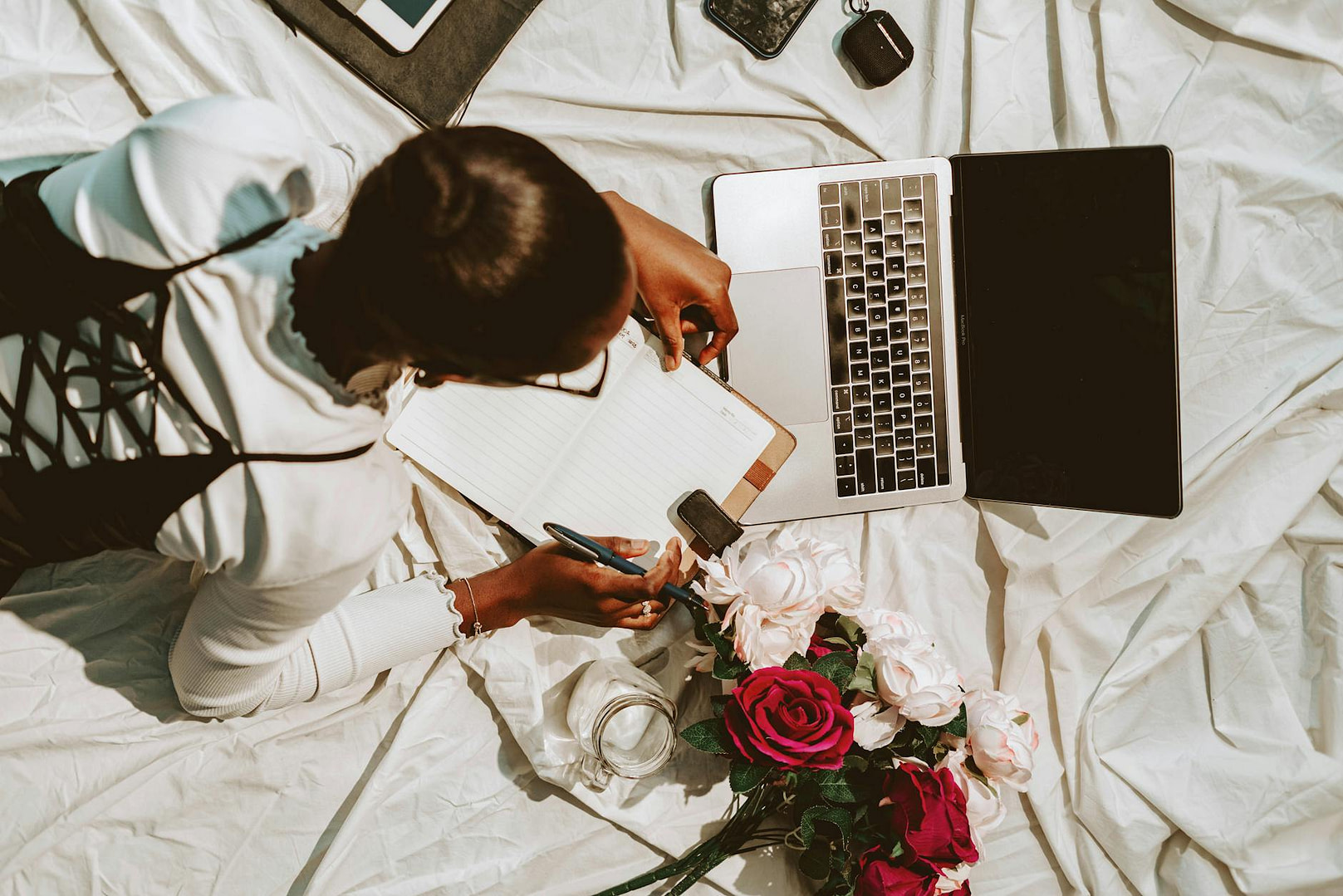a woman is sitting on a bed with a laptop and flowers