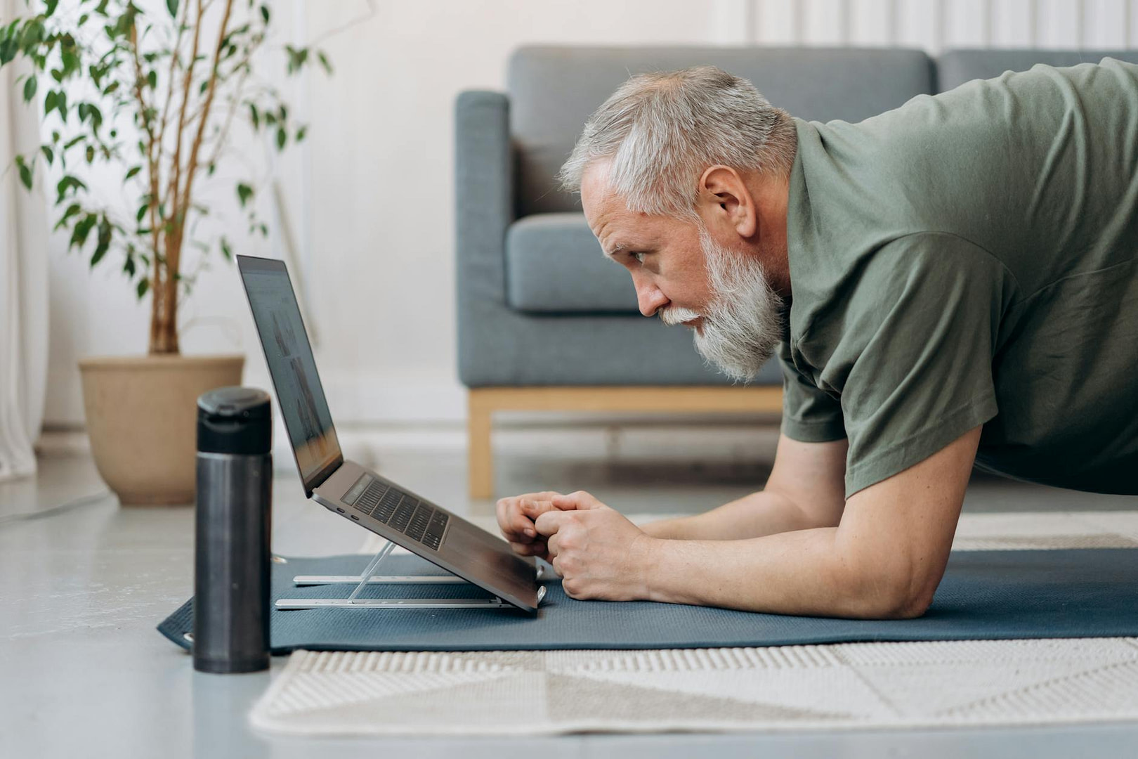 an elderly man working out while looking at the laptop