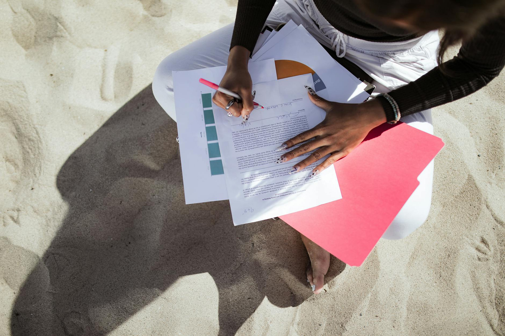 top view of a person signing a document while sitting at a beach
