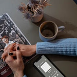A cozy tabletop view featuring a smartphone, magazine, ceramic mug, and a vase of dried flowers.