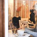 serious young woman using netbook while having hot drink in modern cafe